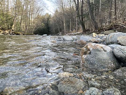 A photo of a ground-level view of a rocky river bed with clear water.