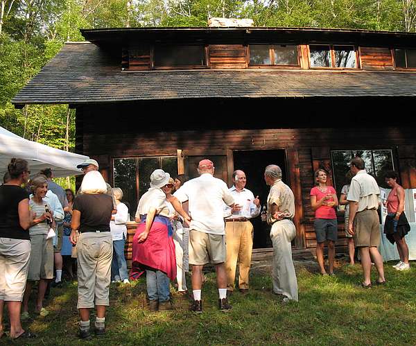 People gathering outside of the Mill Trail Moravian cabin around tables and a pop-up tent.